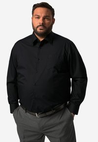 Černá dlouhá košile z hladké tkaniny s límcem na knoflíky, jednou náprsní kapsou a odpovídajícími knoflíky, spojená se šedými kalhotami a opaskem.