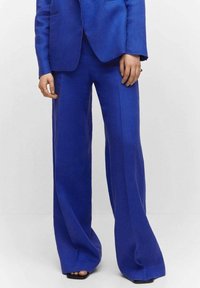 Op maat gemaakte blauwe suit met een getailleerd colbert en wijde broekspijpen, gemaakt van een gestructureerde stof met zijzakken en een gladde revers.
