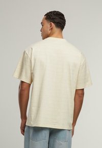 Kreminės spalvos trumpomis rankovėmis marškinėliai su subtiliu raštu. Laisvas kirpimas ir švelni tekstūra, turi apvalų kaklą ir tiesią apatinę dalį.