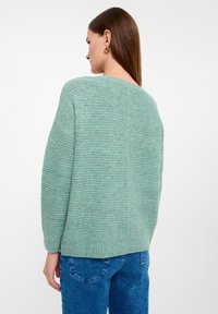 Maglione lavorato a maglia verde menta con un motivo a coste testurizzato, scollatura rotonda e spalle cadute, abbinato a jeans blu.