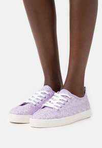 Fioletowe sneakersy z koronkowymi wstawkami, białe sznurówki, teksturowany kwiatowy wzór oraz biała gumowa podeszwa, prezentujące niski profil.