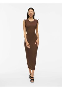 Brą dress w brązowej teksturze, dopasowana, z falbaniastymi akcentami na ramionach, sięgająca do kolan i okrągłym dekoltem, w zestawieniu z czarnymi sandałami na cienkich paskach.