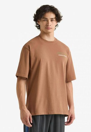 T-shirt in cotone marrone con maniche corte, con un logo stampato in verde. Vestibilità rilassata con scollatura a girocollo, texture liscia.