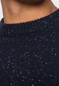 Dunkelblauer gestrickter Pullover mit einem gerippten Rundhalsausschnitt, der über die Stofftextur verstreute weiße und rote Details aufweist.