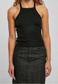Černý žebrovaný halter top s přiléhavým střihem. Hladká textura, bezrukávový styl a zkrácená délka, spojený s tmavými džínovými sukněmi.