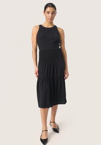Juoda midi suknelė su briaunoto tank top dizainu; surinkta juosmens dalis ir sluoksniuota sijonas. Dėvima su juodais aštriais bateliais. Lygus paviršius.