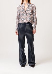 Blouse à manches longues avec un motif floral multicolore et un décolleté en V, associée à un pantalon à rayures bleu marine et des chaussures en cuir marron.