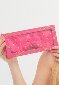 Mascherina per gli occhi in seta rosa con una texture soffice, adornata da piccole cristalli, confezionata in una scatola rosa brillante con motivi geometrici dorati.