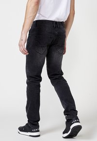 Jeans de denim negro ajustados con un acabado desgastado, que cuentan con dos bolsillos traseros y bordes desgastados. Llevados con zapatillas negras.