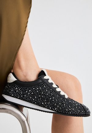 Zapatilla negra con una parte superior texturizada adornada con rhinestones negros, cordones blancos y una suela blanca en contraste.