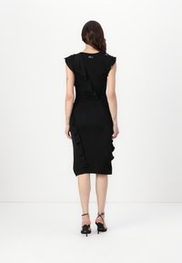Black dress with short ruffled sleeves, fitted silhouette, and side ruffle detail. Paired with black heeled sandals.