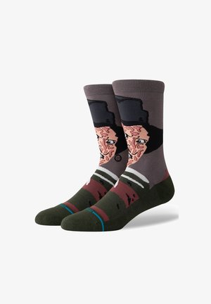 Calcetines de algodón con un diseño gráfico de la cara de un personaje, en una paleta de colores marrón y gris, con un sombrero negro y acentos de rayas verdes.