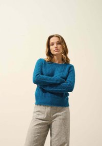 Blå stickad tröja med texturerat diamantmönster, ribbade ärmslut och nederkant. I kombination med ljusgrå texturerade byxor, avslappnad passform.