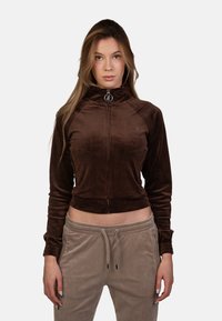 Giacca in velluto marrone con zip, colletto alto, polsini attillati e design cropped, con un logo discreto sul lato sinistro.