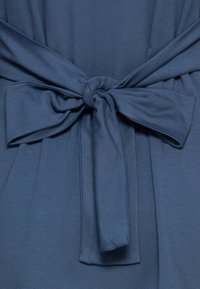 Sininen kangas, jossa on sileä pinta, on varustettu solmittavalla vyöllä, mikä luo ryppyisen vaikutelman. Solmu sijaitsee keskellä, ja molemmin puolin on valuvia kangasta.