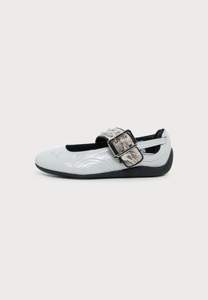 Ballerine blanche avec semelle noire et grande bride à boucle à motif peau de serpent sur le dessus.