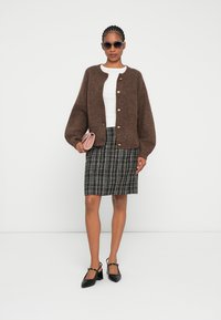 Smeđa pletena kardigan jakna s gumbima, bijeli uski top, karirani mini suknja u crno i bijelo, i crne štikle. Drži malu ružičastu clutch torbicu.