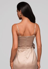 Beżowa, satynowa sukienka z dopasowanym górnym krojem, subtelną, kropeczkową teksturą i cienkimi ramiączkami. Posiada zamek z tyłu i gładką sylwetkę.