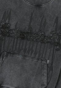 Sudadera negra con un diseño texturizado y bordado que dice "Revolución" en la parte frontal. Cuenta con un cuello de canalé y un bolsillo frontal.