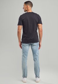 Camiseta de algodón negra, de manga corta, con escote redondo, combinada con jeans de denim azul claro, de corte ajustado y zapatillas blancas.