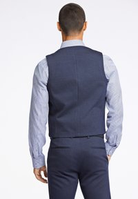 Marineblauer Weste aus strukturiertem Stoff, kombiniert mit einem hellblauen und weißen gestreiften Hemd. Verfügt über einen taillierten Rücken und keine sichtbaren Verschlüsse.