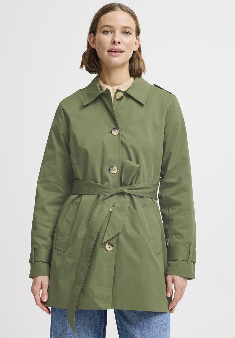 Trench coat verde con cintura alla vita, dotato di grandi bottoni, colletto e tasche laterali. Realizzato in tessuto leggero e morbido.