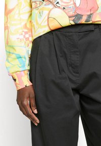 Barevný grafický svetr s volným střihem, zkombinovaný s vysokými černými texturovanými kalhotami, které mají sklady a boční kapsy.