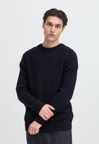 Pulover tricotat de culoare bleu marin, cu un model texturat, guler rotund și mansete și tiv cu elastic, având o croială lejeră și un material moale.