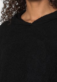 Schwarzer Kapuzenpullover aus strukturiertem, weichem Material. Verfügt über einen rohen Saum und ein lässiges Design mit lockerer Passform.