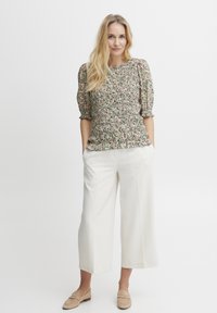 Bluse med blomstermønster og puffede ærmer, indsnævret talje, parret med hvide vidde bukser og beige slip-on sko.