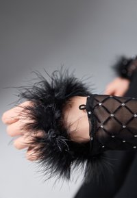 Czarna siateczkowa mankieta z dekoracją z piór, z wzorem w diamenty i małymi cyrkoniami, podkreślająca teksturę i kontrastujące materiały.