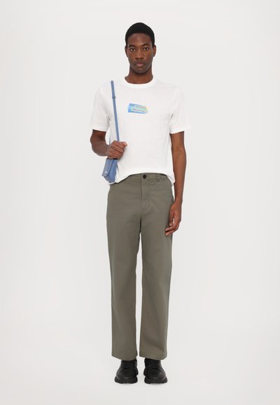 T-shirt blanc avec un graphisme multicolore, pantalon olive, sac à bandoulière bleu clair et chaussures noires. Design simple, coupe décontractée.