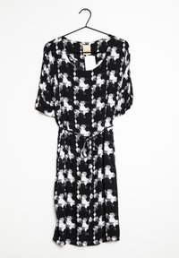 Svart- och vitt mönstrad klänning med korta ärmar, rund hals, dragsko i midjan och en flödande silhuett. Hänger från en svart krok.