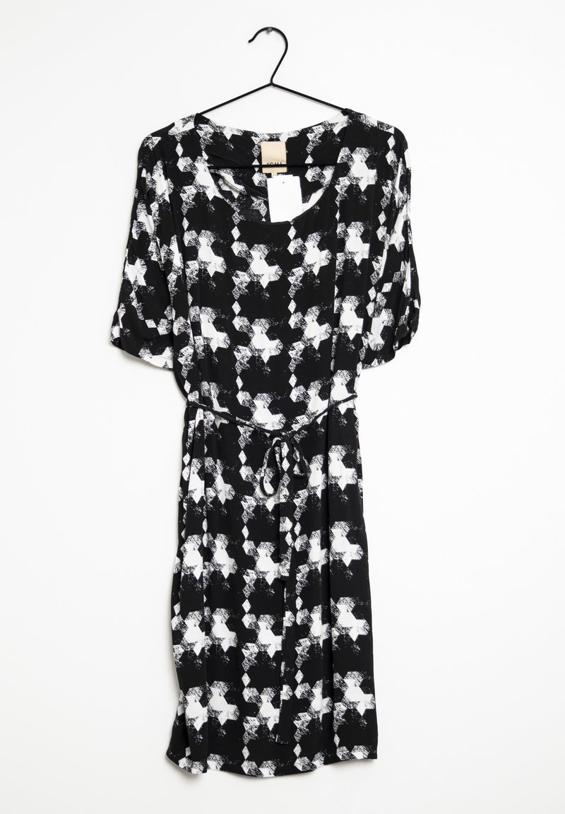 Svart- och vitt mönstrad klänning med korta ärmar, rund hals, dragsko i midjan och en flödande silhuett. Hänger från en svart krok.