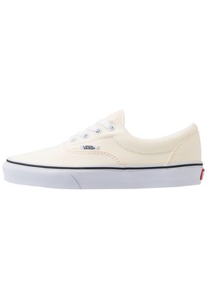 Niskie białe trampki Vans z białymi sznurówkami, czarnym paskiem na białej gumowej podeszwie i metką z logo Vans z boku.