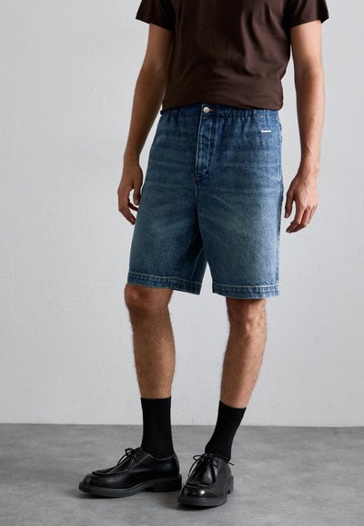 Denim korte broek in middelblauw met een relaxte pasvorm, voorzien van een knoopsluiting en zijzakken. Gecombineerd met zwarte dresschoenen en geribbelde sokken.