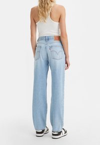 Ljust blå raka jeans i denim, med en bakpatch-label, två bakfickor och en avslappnad passform. Kombinerat med svarta sneakers.