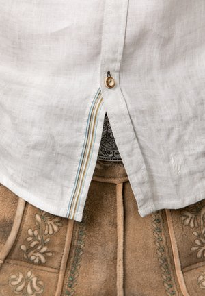 White linen shirt with a rounded hem, featuring a button placket and a multicolored striped accent. Overlaid on tan fabric with floral embroidery.