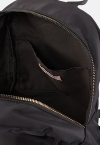 Interior de una mochila negra con un forro de tela suave, cremallera dorada y un pequeño bolsillo etiquetado. Diseño texturizado y minimalista.