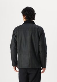 Black, textured jacket with a standing collar and visible seams. Features a button detail at the back and a straight fit.