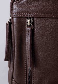 Brown leather bag featuring visible zippers and textured surface, with long zipper pulls and detailed stitching. Close-up view.