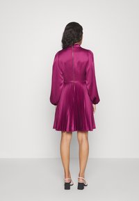 Robe à manches courtes plissée en satin magenta profond avec une fermeture éclair au dos. Dotée d'un col montant et de manches bouffantes.