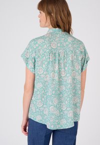 Chemise à manches courtes en turquoise clair avec imprimé floral blanc, dotée d'un col et d'un ourlet arrondi, confectionnée dans un tissu léger.