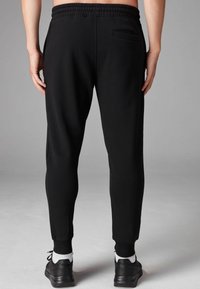 Čierne teplákové nohavice so slim fit strihom, elastickým pásom a detailom zadnej vrecka. Majú rebrované manžety na členkoch a hladkú textúru.