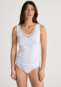 Witte tanktop met een diepe V-hals, voorzien van een kantaccent. De stof is soepel en de pasvorm is aansluitend. Gecombineerd met bijpassend wit ondergoed.