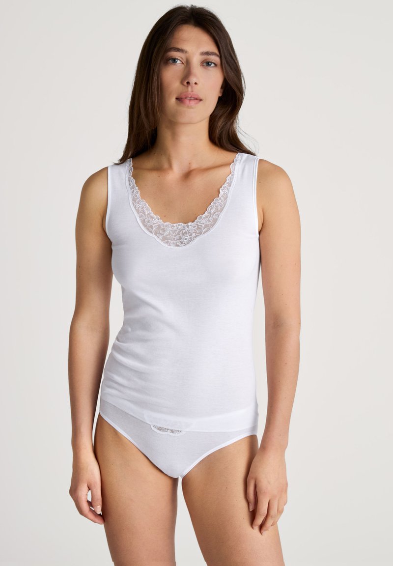 Witte tanktop met een diepe V-hals, voorzien van een kantaccent. De stof is soepel en de pasvorm is aansluitend. Gecombineerd met bijpassend wit ondergoed.