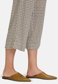 Bruine leren instap schoenen met een spitse neus, gecombineerd met een broek met patroontjes die geometrische vormen in aardetinten en wit vertonen.