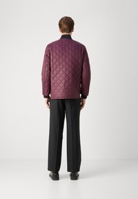 Quilted jacket in deep burgundy, featuring a diamond pattern, long sleeves, and a black collar. Paired with black wide-leg pants and shoes.