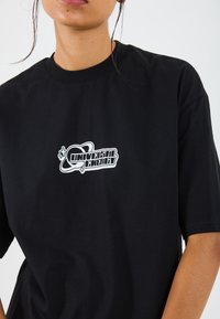 Camiseta negra de algodón con cuello redondo, que presenta un logo gráfico blanco de "Energía Universal" en el pecho. Mangas cortas.