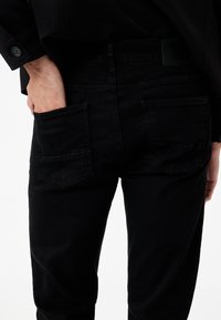 Schwarze Denim-Jeans mit Gesäßtaschen und dezenten Nähten. Der Stoff hat eine glatte Textur und ein figurbetontes Design.